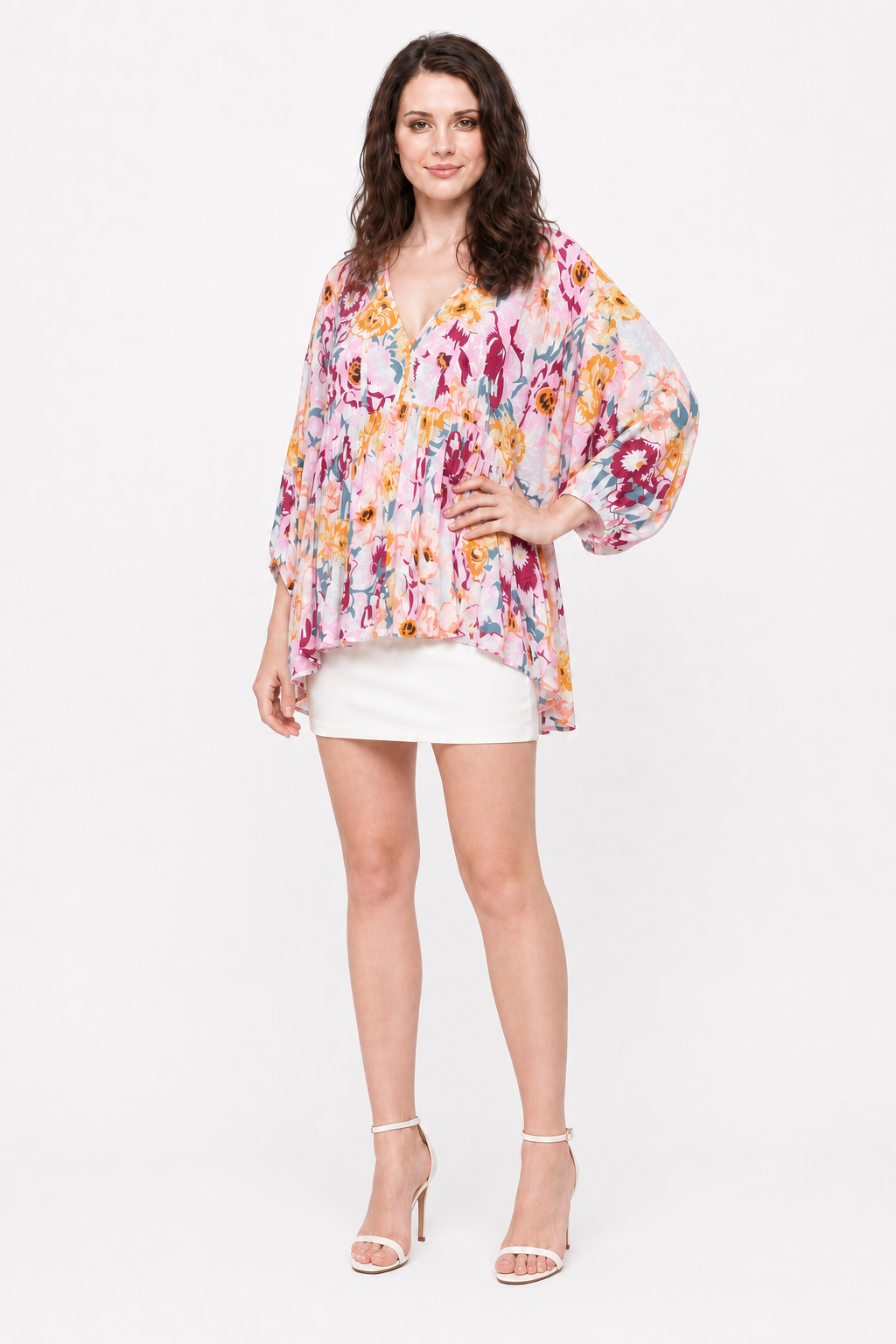 Zena wearing The Layla Floral Top with a white mini skirt and white strappy heels, three-quarter view.