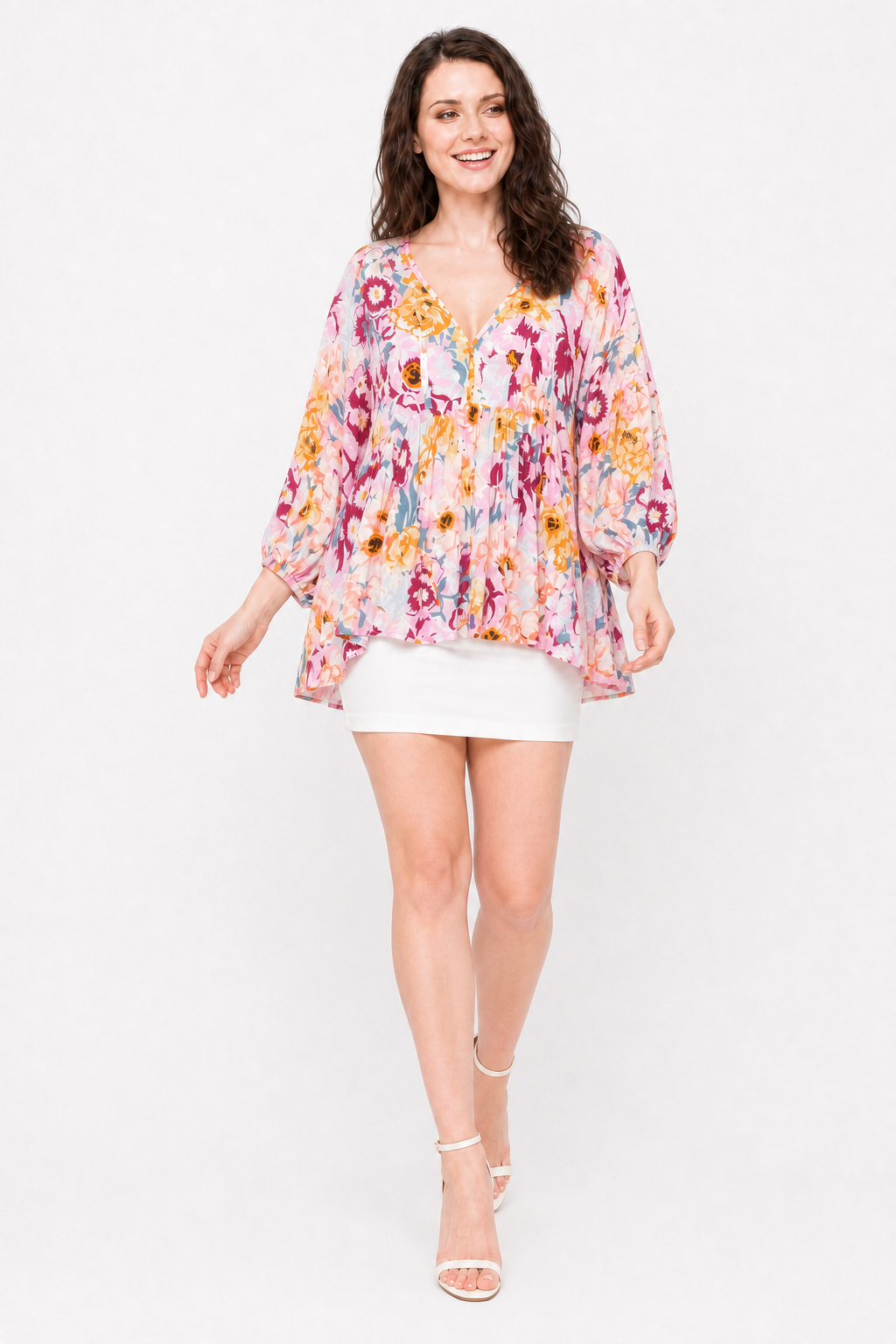 Zena walking in The Layla Floral Top with a white mini skirt and white strappy heels, smiling.