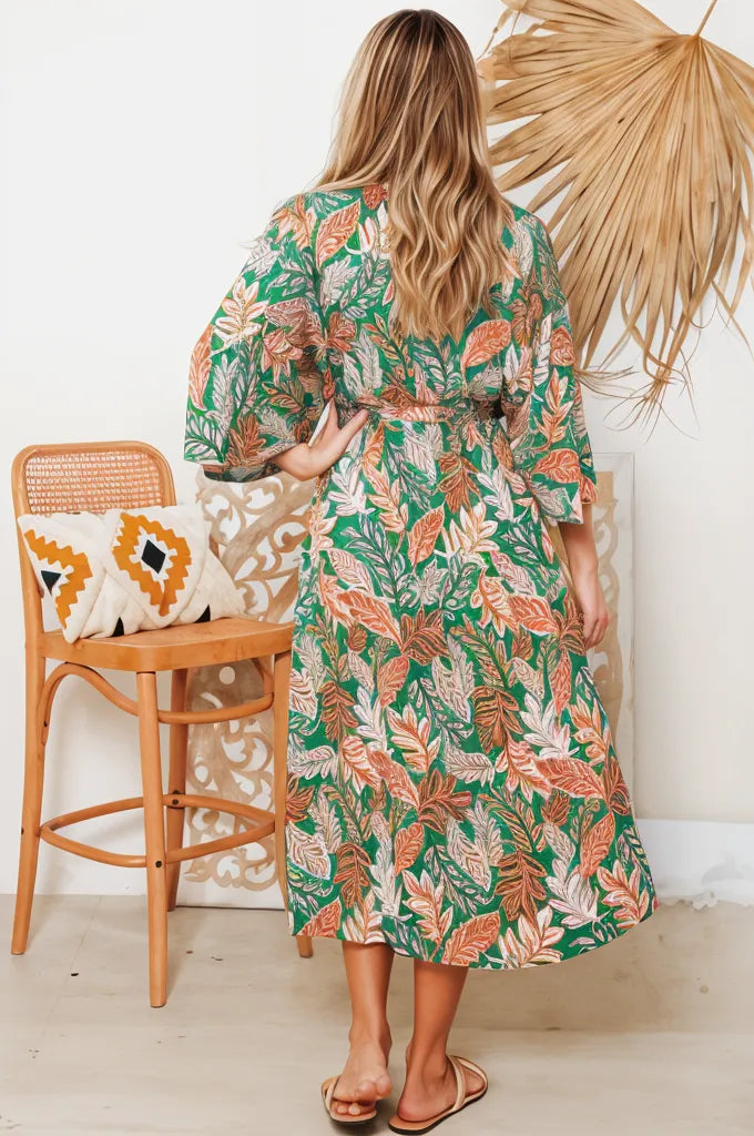 Back view of Ziana Heena floral dress with green, orange, and pink leaves pattern worn by woman indoors